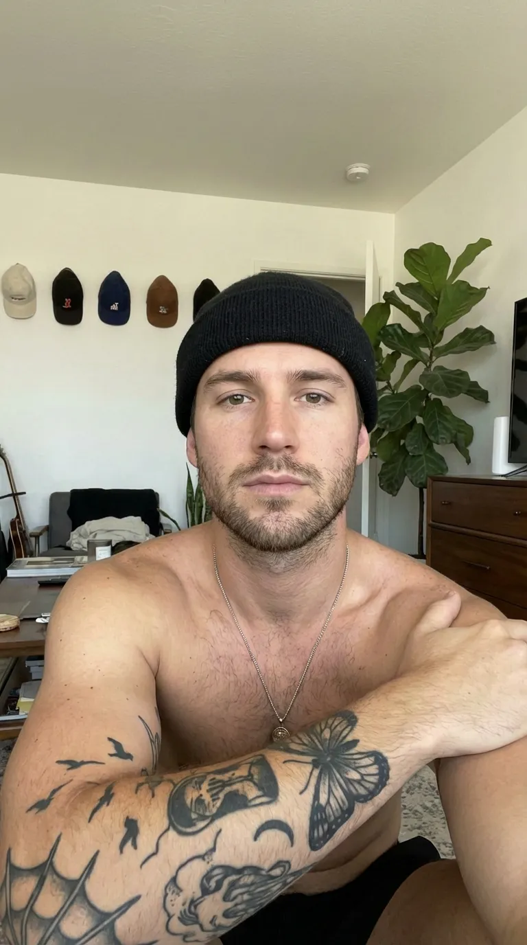 Retrato de ejemplo: hombre con gorro negro y brazo tatuado sentado en una habitación luminosa con una planta